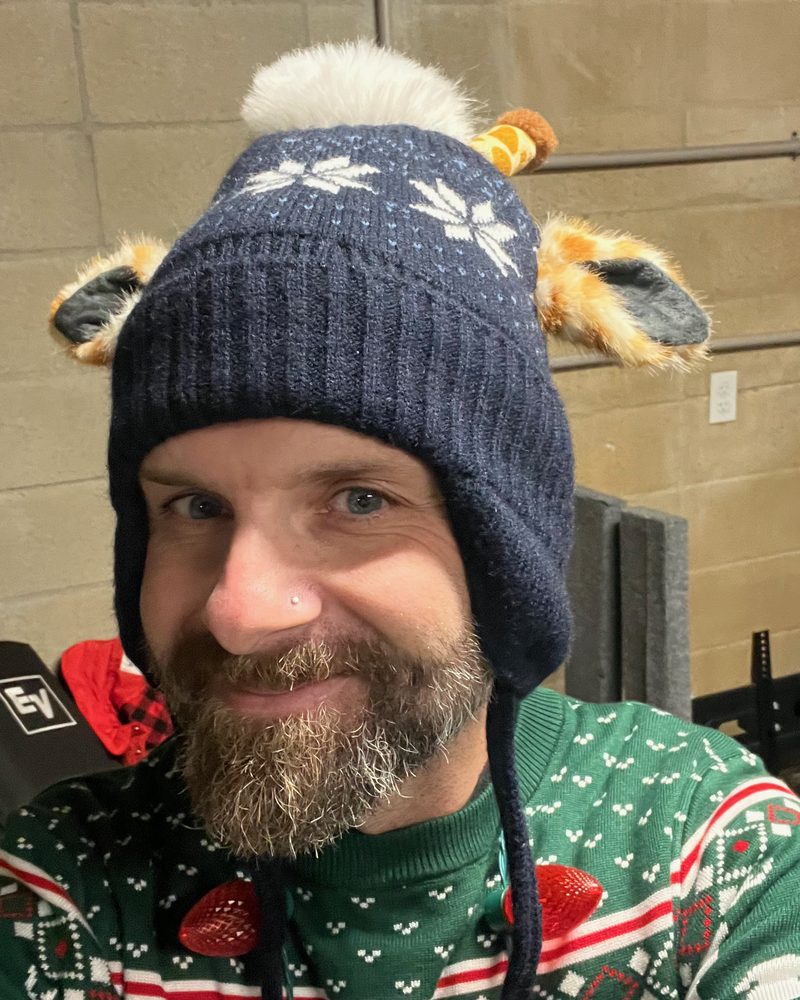 davyrockett smiling in a giraffe-eared winter hat and holiday sweater